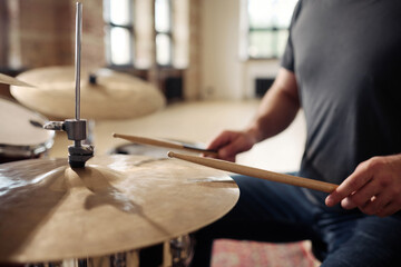 Close-up of man holding drumsticks and learning to play drums at drum kit at studio