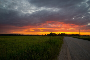 Naklejka na ściany i meble Scenic rural landscape with rural broken dirt road at sunset.