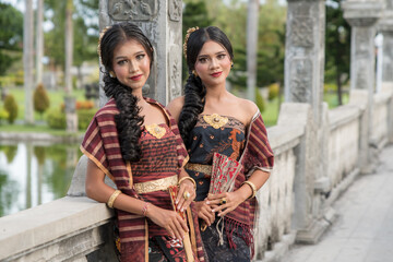 Beautiful girls in Balinese traditional dress with fan, Taman Ujung Bali. - obrazy, fototapety, plakaty