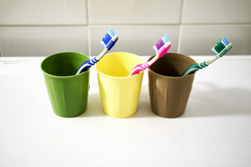 three colorful toothbrushes in colorful mugs on the bathroom table