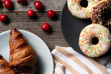 Freshly baked french croissant and colorful glazed donuts exposed on the decorative platter with juicy cherries