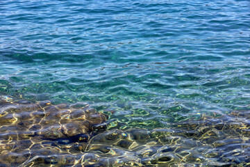 Transparent sea surface with stones on a bottom. Turquoise water for background