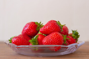 Many red strawberries on glass plate and wooden table top view