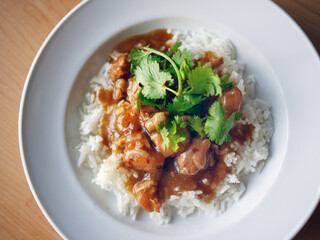 close-up chicken in brown sauce chinese style over rice cover with coriander in white plate