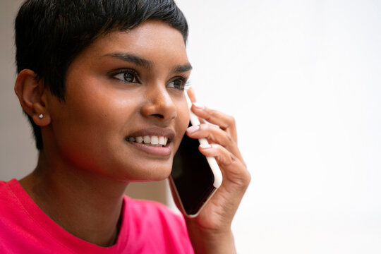 Closeup Portrait Of Smiling Indian Woman With Stylish Short Hair Talking On Mobile Phone Looking Away, Copy Space 