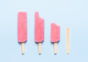 Pink popsicle ice cream on wooden stick consumption life cycle on blue background top view flat lay