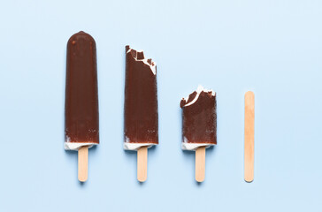 Chocolate covered ice cream on wooden stick consumption life cycle on blue background top view flat lay