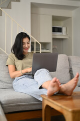 Relaxed young woman watching videos, surfing internet, shopping online on laptop computer in living room