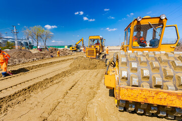 Road roller with spikes and earthmover are working at construction site
