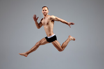 Fototapeta na wymiar Full length portrait of a confident young sportsman shirtless jumping isolated over white background