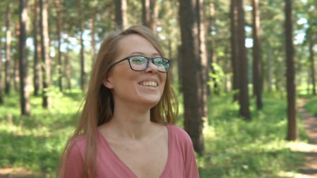 Woman enjoying summer day vacation in the forest park. The face of a smiling, laughing and happy girl with glasses in outdoors travel. Sunny day woods holiday journey. 
