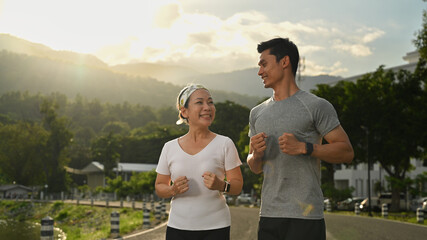 Active healthy mature woman jogging at the park with her personal trainer. Healthy lifestyle and fitness concept
