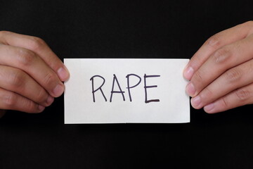 Rape case or sexual assault mug shot concept. Criminal hands holding paper placard with written...