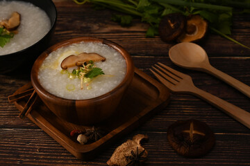 Rice porridge, rice gruel or congee with shiitake mushroom, slice ginger and scallion served in wooden bowl for light meal