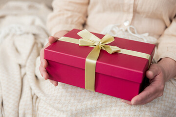 Red gift box beautifully wrapped with gold ribbon held in woman's lap. Mother's day, birthday, occasions.