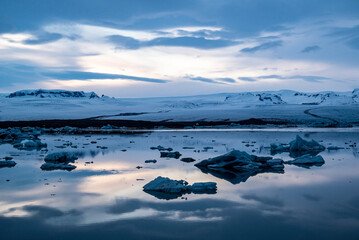 Tranquil scene at Jökulsárlón glacier lagoon during the blue hour, a dramatic sky reflected in the water, Breiðamerkurjökull in the background, Vatnajökull National Park, Route 1 / Ring Road, Iceland