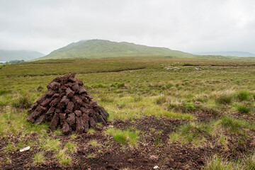 Turf field in country side. Connemara, Ireland. Traditional fossil fuel for burning in a stove and cooking. Old traditional way to heat a home or household. Mountains and cloudy sky in the background