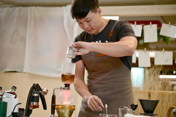 Closeup of Asian Male Barista using a coffee machine in a coffee shop to make coffee for customers to order inside a coffee shop cafe in Thailand.