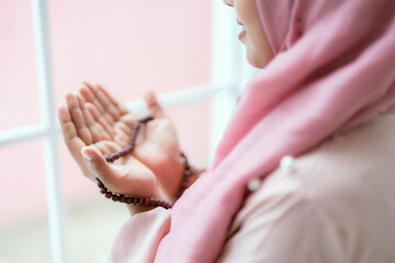 Young muslim woman with rosary praying with closed eyes at home