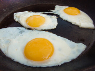 3 fried eggs frying in a pan with olive oil. Three fried eggs in cast iron frying pan sprinkled with ground black.
