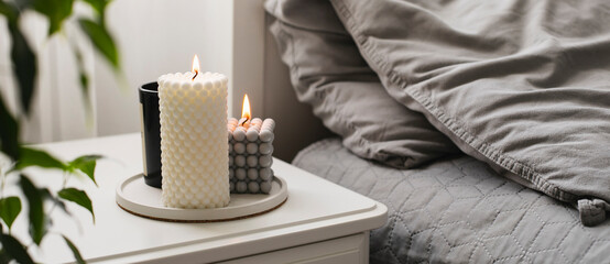 Modern burning candle on bedside table near bed. Home aroma. Wellness. Banner image for design