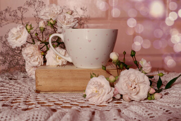  Good summer morning wishes: a cup of tea stands on a book, a bouquet of delicate roses, a lace napkin, bokeh, space for text
