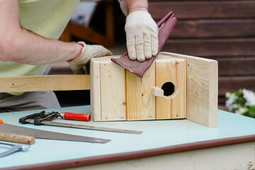Close up of craftsman making a wooden birdhouse with tools. DIY concept. Carpenter polishing...