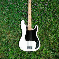 Details of a white electric bass guitar on the grass.