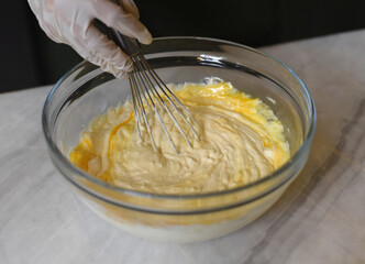 A hand in rubber glove stirring 
dough for a cake  