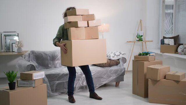 man with cardboard boxes loses his balance and slowly falls on sofa covered with oilcloth, problems when moving to new apartment