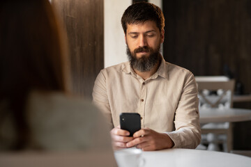man and woman colleagues drinking coffee in cafe, guy using smartphone sitting at table in coffee break, no free time
