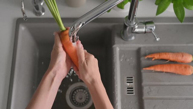 Slow motion footage of woman washing young fresh carrots in kitchen sink under tap water. Natural organic products vegetables, healthy food. Stylish modern kitchen. Concept of cooking at home