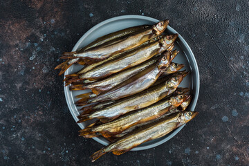 Smoked capelin on a round light plate on a dark background.