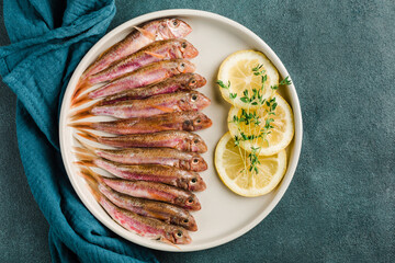 Some fresh Black Sea red mullet on a white plate with a slice of lemon and thyme on a blue background.