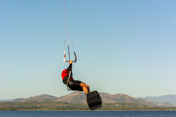 Expert Kitesurfer Jumping a Back Roll with  Sea Watrer Splashes during Golden Hour on Blurred Green...