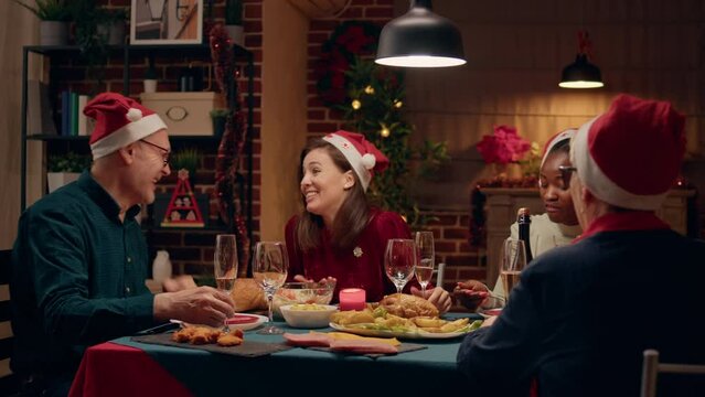 Beautiful woman laughing and talking with senior father-in-law while enjoying Christmas dinner at home. Festive family members relaxing together while conversating and eating home cooked food.