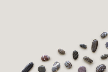 Minimal flat lay with sea pebble stones on beige background with copy space. Natural smooth stone black color. Summer concept, empty space