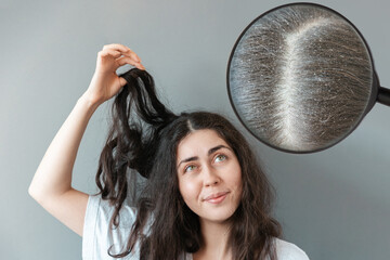 Young woman holds a tangled strand of her hair in bewilderment. Zoomed hair parting area with...