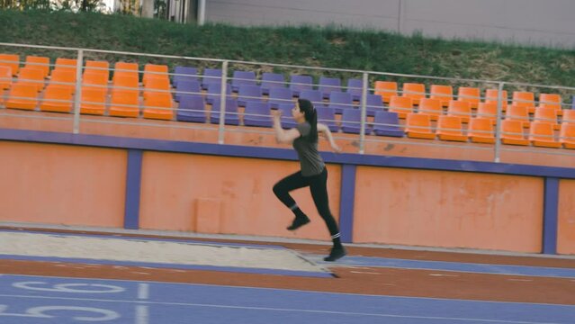 A Sporty Runner Athlete Woman Runs Up At A Stadium And Performs A Long Jump In Slow Motion In A Stadium 