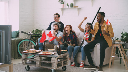 Multi ethnic group of friends sports fans with Canadian national flags watching hockey championship...
