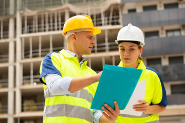 Man and a woman working at a construction site discuss a construction plan, holding an estimate in their hands