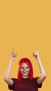 Vertical video. Special offer. Look here. Great opportunity. Happy excited woman pointing up presenting something invisible on yellow copy space commercial background.