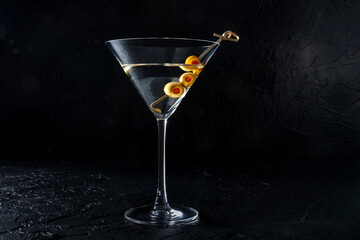 Martini, a glass with spicy olives on a toothpick, on a black background. Alcoholic drink