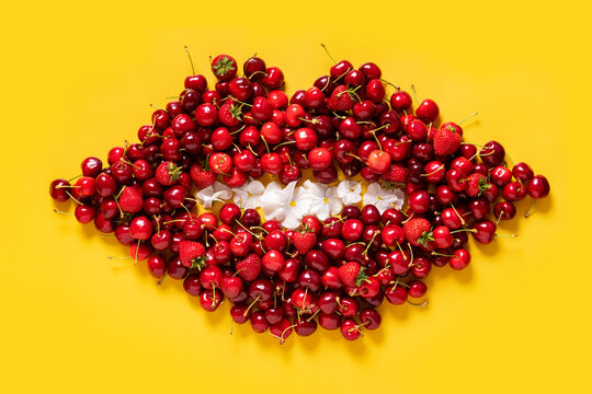 Cherry and strawberry red fruits pattern in a shape of a mouth on bright yellow background