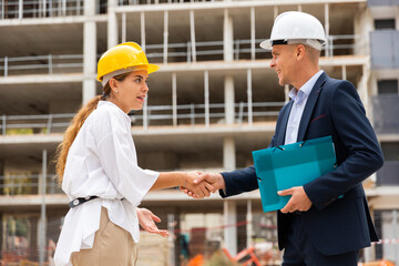 Young woman client shaking hand with builder after finishing signing contract at construction site