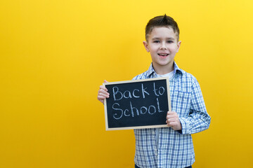 schoolboy holding a tablet in his hands with the inscription Back to school on a yellow background.