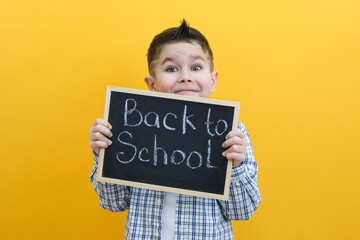 schoolboy holding a tablet in his hands with the inscription Back to school on a yellow background.