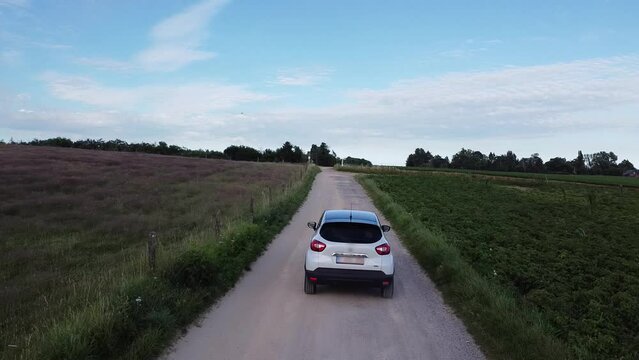 White car driving slow on a dirt road between the farm fields in Scherpenheuvel, Belgium.
