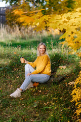 Stylish confident woman walking in the park fall. Modern autumn outfit. Girl drinking coffee to go Sunny warm day in the city. Good beautiful weather. Cozy trendy yellow sweater. enjoying the weather