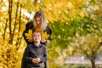 Mother and son have fun together. Family walk in the park in autumn. Hello October. Thanksgiving holiday. Happy motherhood. Childhood. Maple leaves. Fun play together. Leaf ears. Fall